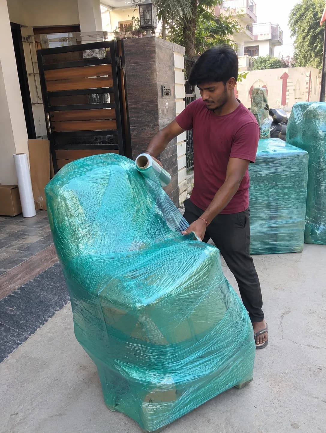 Agarwal Packers and Movers crew member stretch-wrapping an armchair in protective film during packing at a Dehradun home