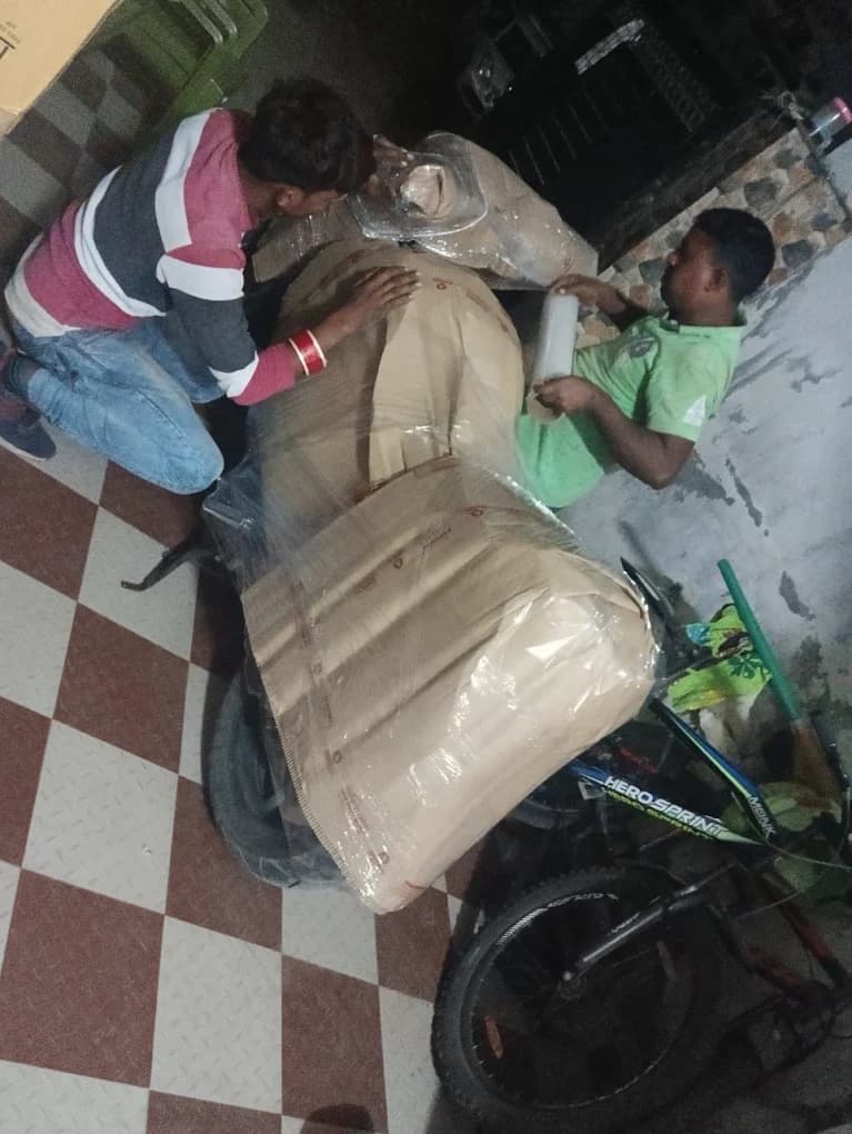 Two Agarwal Packers and Movers workers wrapping a motorcycle in protective material before transport from Dehradun